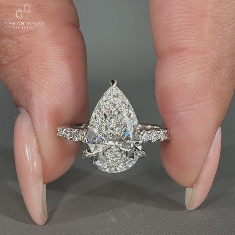 Pear diamond ring featuring three claw prong setting and round side stones.
