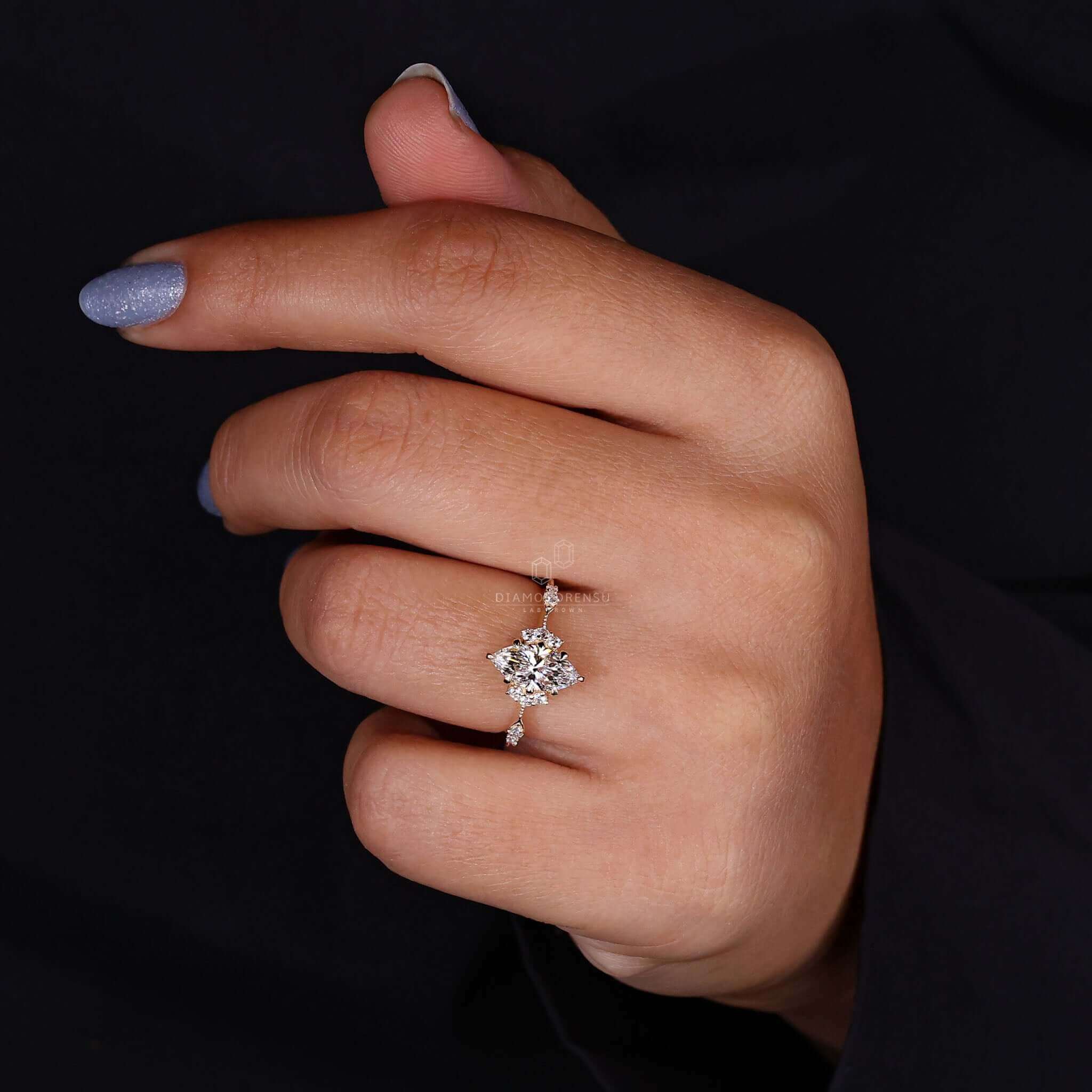 Woman's hand showing off a marquise cut engagement ring with a lab-grown diamond, featuring sidestones and claw prongs.