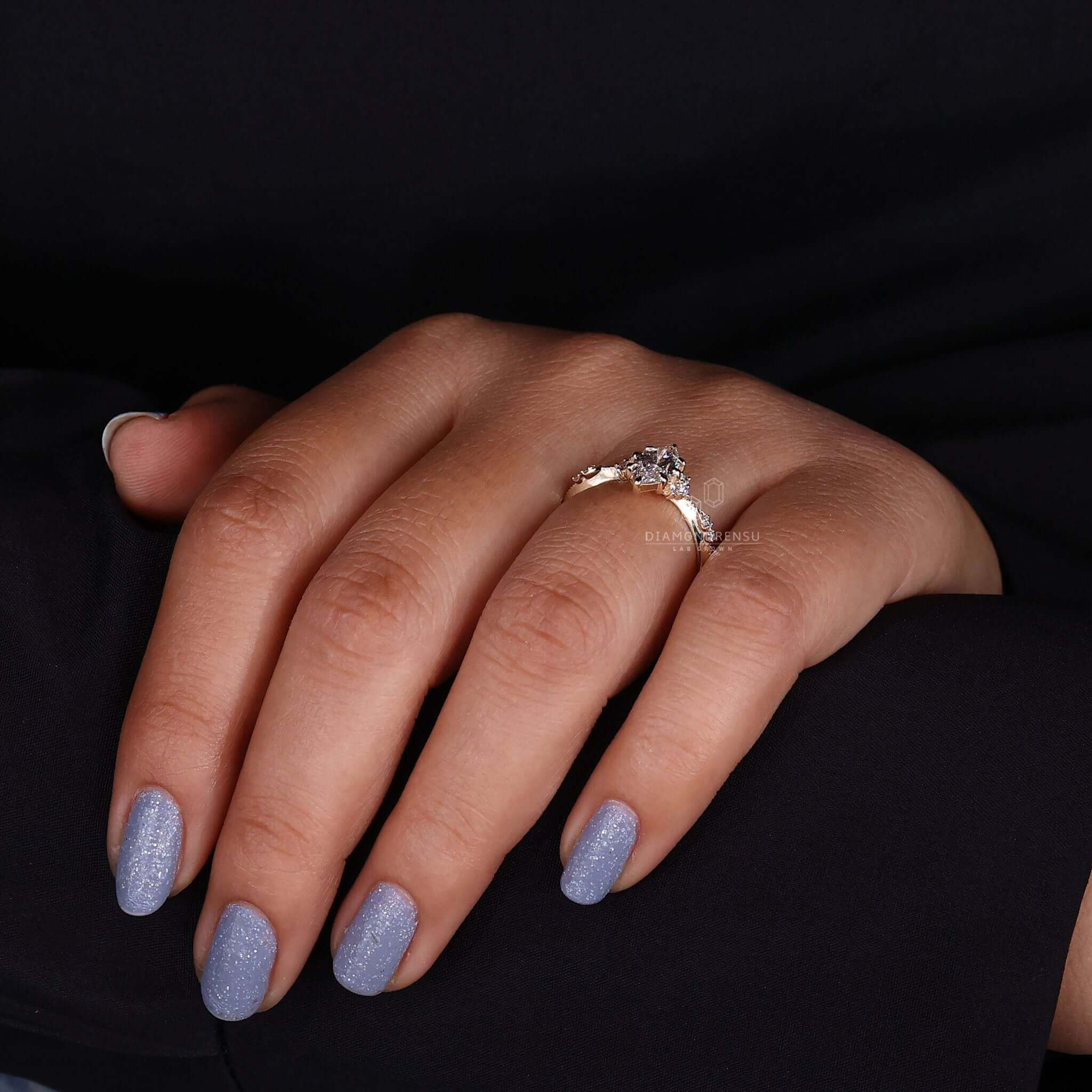 Woman's hand showing off a marquise cut engagement ring with a lab-grown diamond, featuring sidestones and claw prongs
