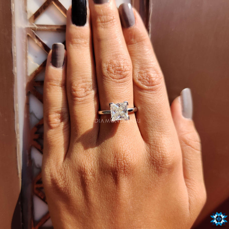 Princess cut engagement rings on finger, showcasing the brilliance of handmade jewellery.